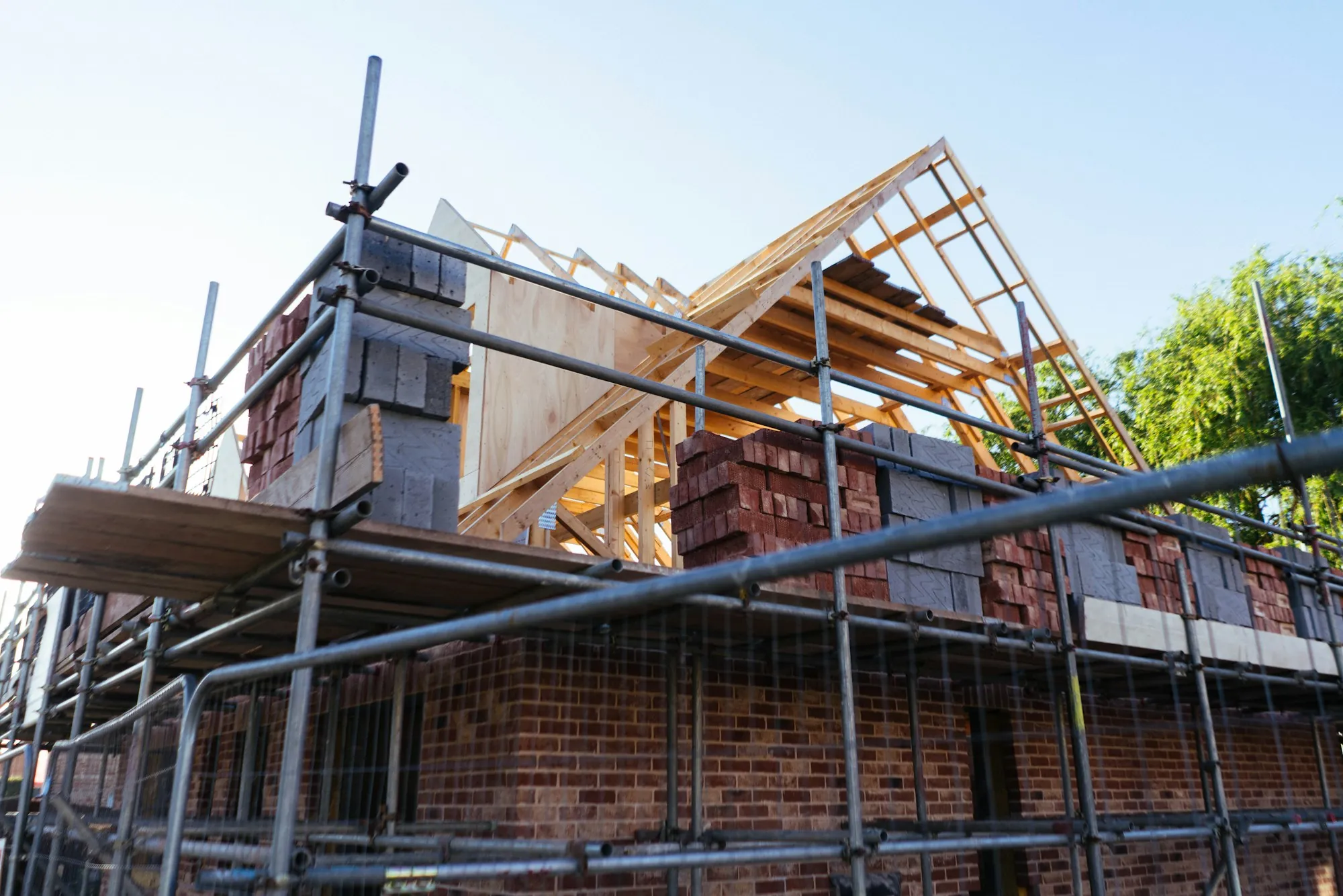 New roof framing and brick walls of a home addition surrounded by scaffolding